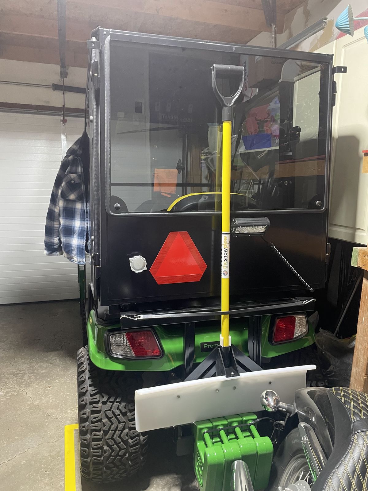 The rear of the cab tractor in a garage, with a snow shovel mounted on the back