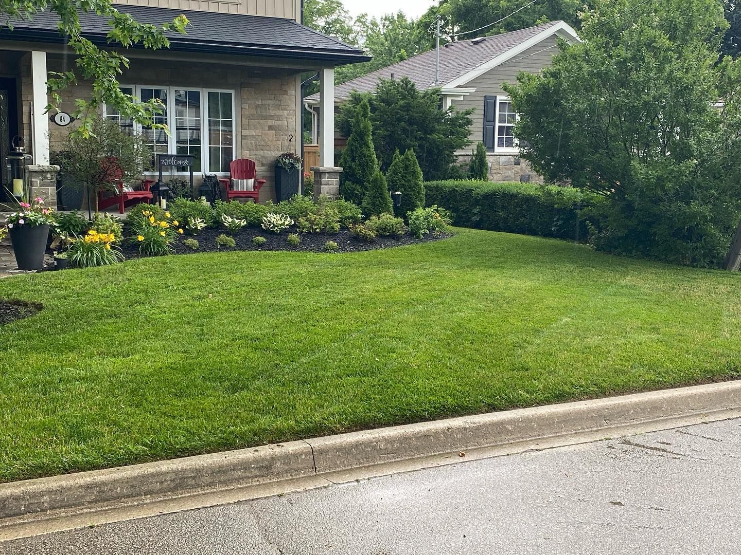 A freshly cut front lawn and planted beds in front of a stone house